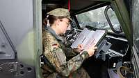 Eine Soldatin sitzt in einem Bundeswehr Fahrzeug und schreibt etwas mit einem roten Stift auf einer Liste. 