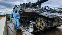 Eine Panzerhaubitze wird von einem Soldaten in Schutzkleidung eingesprüht.
