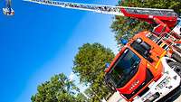 Ein Feuerwehr-Löschfahrzeug steht auf einem freien großen Gelände und hat seine Drehkranleiter mit Rettungskorb ausgefahren