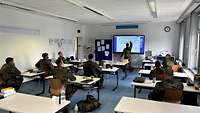 In einem Klassenzimmer sitzen Soldaten und hören dem Lehrer an der Smartboard zu.