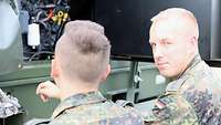 Zwei Soldaten stehen vor einem Stromerzeuger. Der Soldat auf der rechten Seite sieht Richtung Kamera.