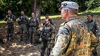 Mehrere Soldaten stehen im Wald bei sonnigem Wetter in einer Gesprächsrunde.