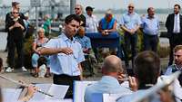 Ein Soldat steht als Dirigent vor einem Orchester.