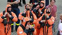 Fünf Personen legen einen orangenen Schutzanzug an.