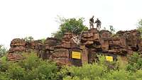 Drei Ortsschilder hängen an einem Berg in Mali. Zwei Soldaten schauen die Schilder an.