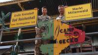 Zwei Soldaten präsentieren jeweils ein Ortsschild