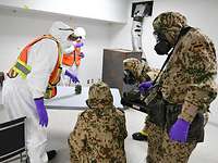 Fünf Soldaten in Schutzanzügen und mit ABC-Schutzmaske stehen um ein Behältnis auf einem Tisch und besprechen sich.