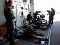 Drei Verletzte im Hangar eines Schiffes mit mehreren Helfern drumherum.