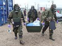 Aufbruch des SIBCRA-Teams Soldaten in Schutzanzügen und mit ABC-Schutzmasken laufen mit ihrer Ausrüstung über ein Übungsgelände.