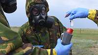 Mehrere Soldaten testen auf offenem Gelände mit Messgeräten die Zusammensetzung eines Kampfstoffes