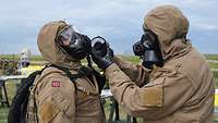 Ein Soldat wechselt den Filter von der Gasmaske eines anderen Soldaten aus