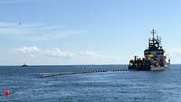 2 Schiffe bringen Ölsperren auf dem Wasser aus.