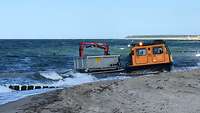 Ein Mehrzweckfahrzeug mit Ketten fährt am Strand entlang und transportiert Gegenstände.
