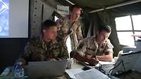 Ein deutscher, ein norwegischer und ein niederländischer Soldat arbeiten an Laptops in einem Zelt.
