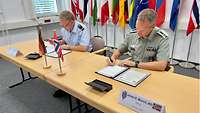 Two soldiers sitting at a table each sign on a piece of paper