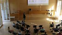 Mehrere Personen sitzen in einem Seminarraum und schauen auf eine PP-Präsentation
