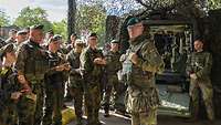 Ein Soldat mit grünem Barett steht vor einer großen Gruppe von Soldaten, die auf ihn schauen.