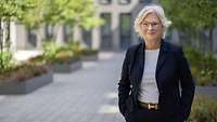 Portrait der Ministerin, die in einem sonnigen Hof steht.