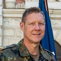 Ein General steht neben aufgestellten Flaggen und schaut freundlich in die Kamera.