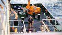 Ein Mann beweg mit einem Hubwagen Kisten auf einem Schiff 