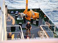 Ein Mann beweg mit einem Hubwagen Kisten auf einem Schiff 