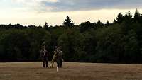 Auf einem Feld stehen zwei Soldaten mit Vermessungsgeräten.