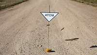 Ein dreieckiges Warnschild mit der Aufschrift „Atom“ auf der Straße.
