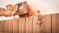 Schutzwall Ein Radlader befüllt eine Begrenzungsmauer mit staubigem Sand