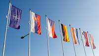 Flaggenmasten vor blauem Himmel mit Flaggen der NATO, SVK; CZE, DEU, NDL, SVN und USA.