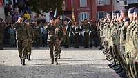 Zahlreiche Soldaten stehen auf einem Platz in Formation. Soldaten schreiten die Front ab.