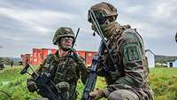 Zwei Soldaten knien mit ihren Waffen auf einer Wiese und unterhalten sich.