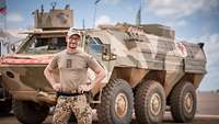 Ein Soldat steht vor einem gepanzerten Fahrzeug