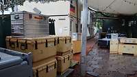 Mehrere Kisten stapeln sich auf dem Platz zwischen Containern