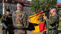 Ein Soldat mit Handschuhen hält eine Truppenfahne. Ein anderer entfernt davon das grüne Fahnenband.