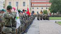 Angetretene Soldaten schauen nach links, einige grüßen militärisch, ein Musikkorps marschiert ein.