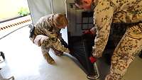 Eine Soldatin und ein Soldat umwickeln eine Box mit schwarzer Folie
