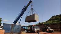 Ein Kran hebt einen Container auf die Ladefläche eines LKW