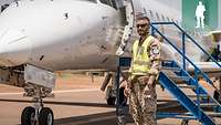 Ein Soldat mit Warnweste steht vor einem zivilen Flugzeug