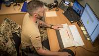 Ein Schreibtisch mit Rechner, Telefon und Soldat davor
