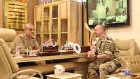 Ein deutscher Soldat sitzt einem irakischen Direktor am Schreibtisch im Gespräch gegenüber, rechts Sofa und Couchtisch 