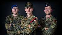Portrait of three servicemen against a black background looking into the camera with their arms folded
