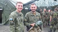 Zwei kosovarische Soldaten stehen vor einem Zelt und lächeln in die Kamera