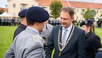 Mehrere Soldatinnen und Soldaten und eine Mann mit einer goldenen Kette geben sich die Hände