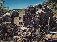 Mehrere KSK-Soldaten versorgen einen am Boden liegenden verwundeten Soldaten im Gelände.