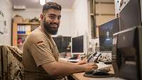 Ein Soldat arbeitet an einem Arbeitsplatz mit Computer, Drucker und Telefon