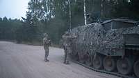 Zwei Soldaten sprechen mit einem dritten Soldaten auf einem Panzer
