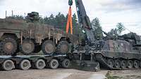 Ein Panzer mit Kran setzt einen anderen Panzer auf einem Tieflader ab