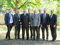 Dr. Bieber und die Festredner Acht Männer, drei in Uniform und fünf in zivilem Anzug, stehen im Freiem und lächeln in die Kamera.