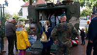 Zivilisten schauen sich einen Radpanzer an, dessen Heckklappe geöffnet ist. 