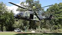 In einem Park auf einer kleinen Rasenfläche zwischen Bäumen landet ein Hubschrauber.